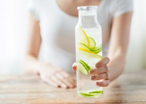 woman holding glass of infused water with lemon and cucumber slices