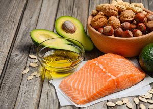 A spread of foods with healthy fats including salmon, olive oil, nuts, and avocado
