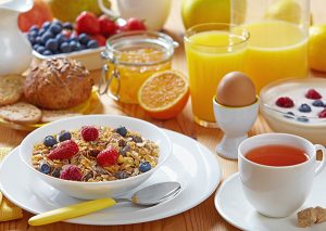 A breakfast spread of muesli topped with fresh fruit, breads, a hard boil egg, yogurt, berries, and orange juice