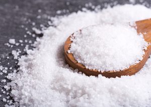 A pile of kosher salt with a wooden spoon heaped with salt on top
