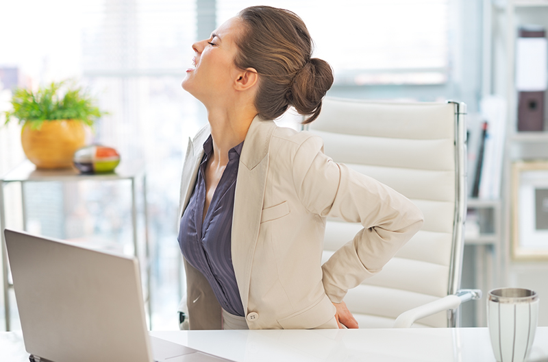 Woman sitting at desk with lower back pain holding her back in agony