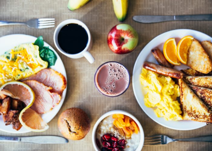 top down view of breakfast plates filled with eggs bacon, fruits, toast, coffee, and juices