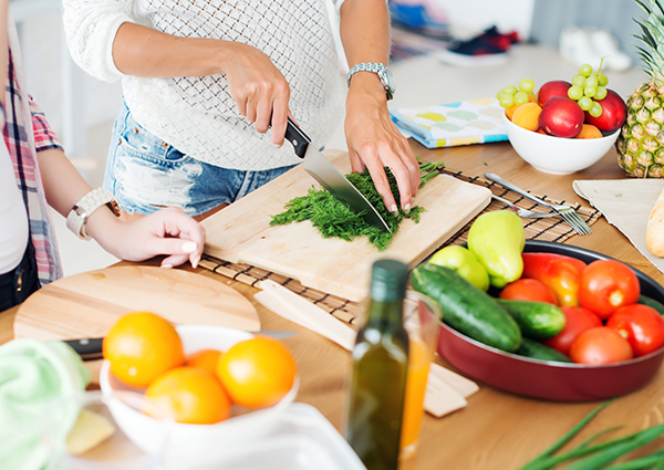 Woman cutting up parsley on a cutting board on her kitchen counter filled with fresh fruits and vegetables