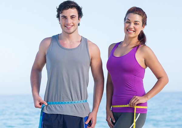 Male and female running partners on the beach holding measuring tapes around their waist