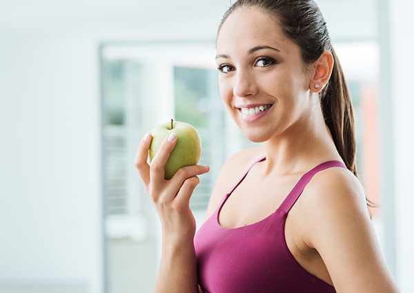 Young woman holding a green apple and smiling in her house