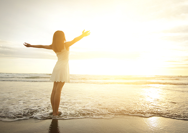 woman standing on a beach with open arms as the sun sets