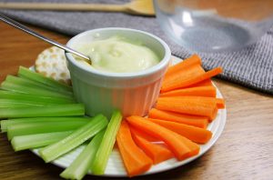 Ramikin of mayonaise on a plate with sticks of celery and carrot, as well as some crackers