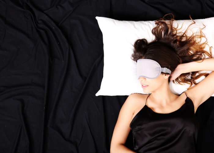 Woman with black bedsheets sleeping on a white pillow with white eyeshades
