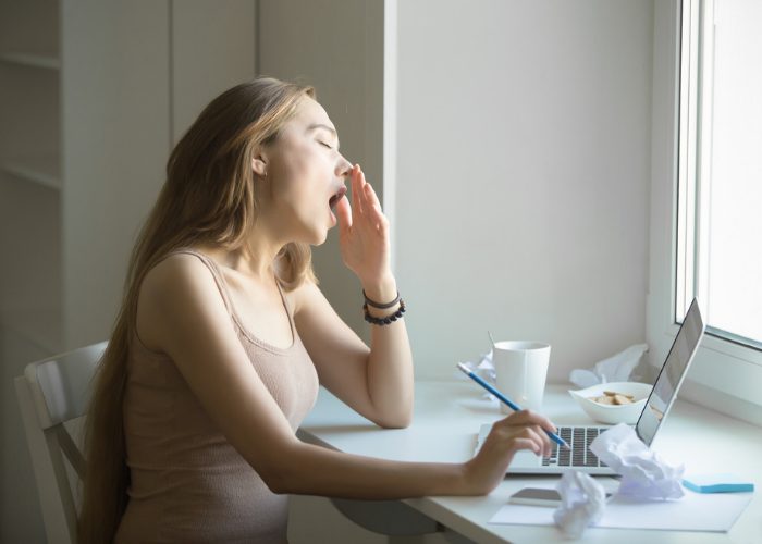 Woman trying to do work in the middle of yawning due to sleep deprivation 