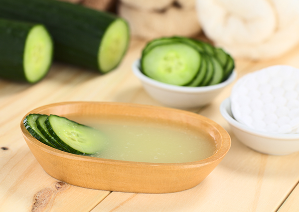 Fresh slices of cucumber in a wooden bowl with whole cucumber in the background ready to make a DIY cucumber face mask