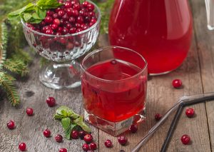 Glass of fresh cranberry juice in front of a bowl of whole cranberries and a jug of cranberry juice