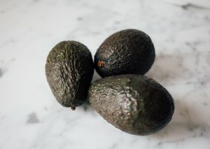 three ripe avocados on a marble cutting board