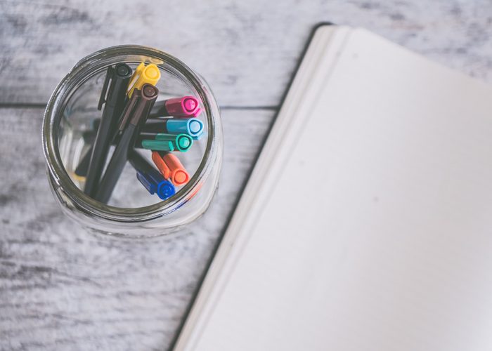 jar of colored pens next to an open notebook