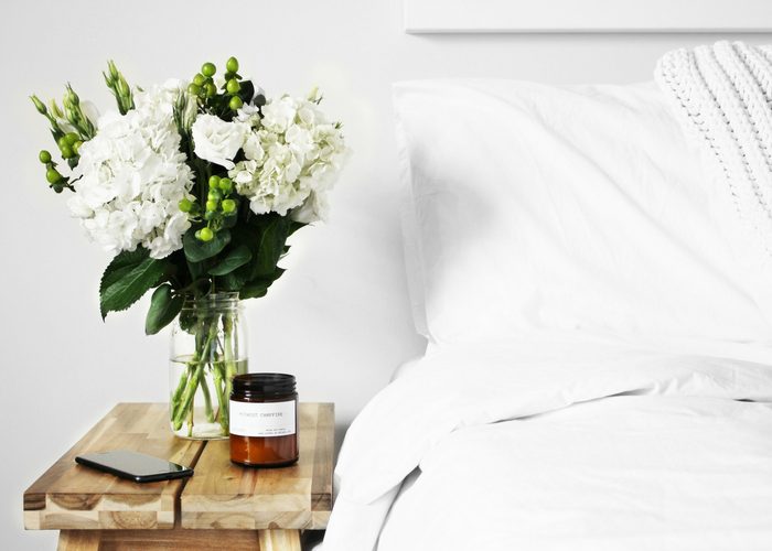 vase of white flowers next to a bed with white linens