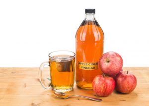 bottles of filtered apple cider vinegar with three red apples and a cup of tea