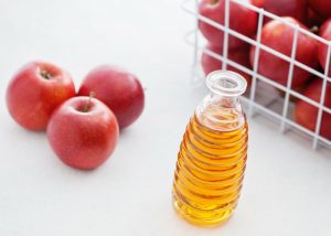 a bottle of apple cider vinegar with a basket of apples on a white background