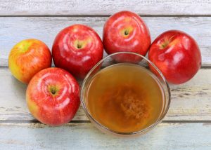 bowl of unfiltered apple cider vinegar including the mother and five red apples
