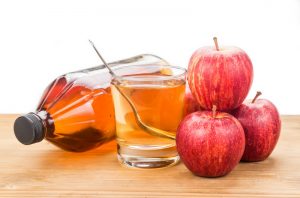 A bottle of apple cider vinegar with an apple cider vinegar drink and 4 red apples