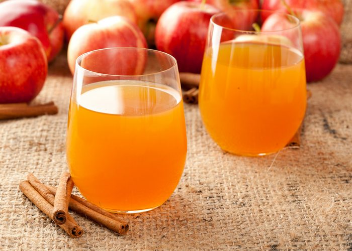 two glasses of apple cider vinegar drinks with red apples and cinnamon sticks