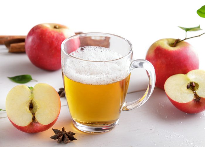 a frothy apple cider vinegar drink in a glass with red apples around it