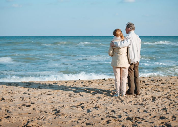 an old couple standing on a beach looking at the sea
