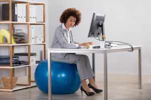 Woman in a suit sitting on an exercise ball at her desk in her office