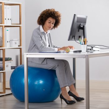 Woman in a suit sitting on an exercise ball at her desk in her office