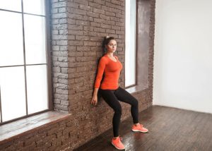 young woman in bright orange workout clothes doing wall sits