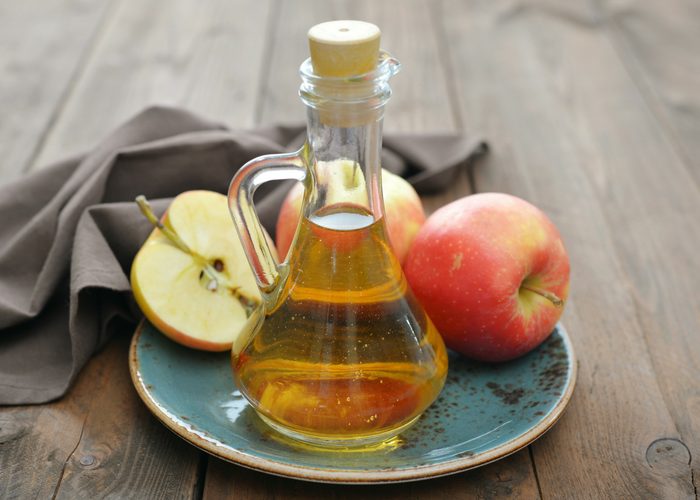 a bottle of apple cider vinegar and apples sitting on a blue dish