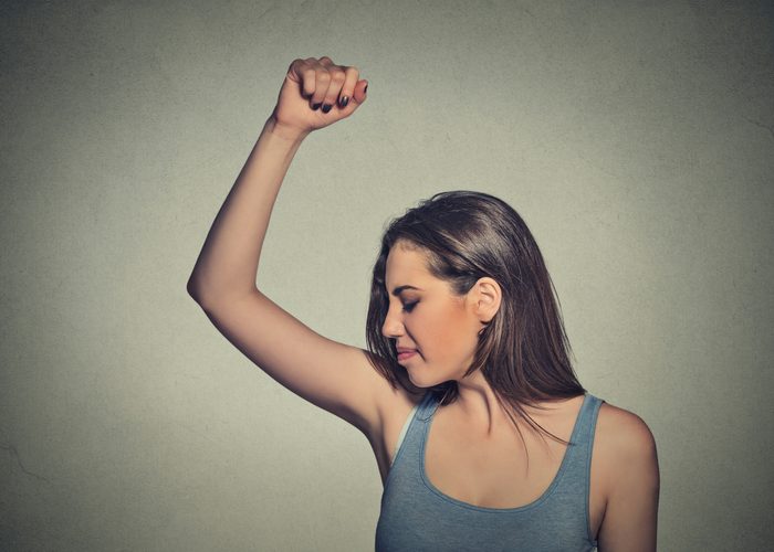 woman with raised fist smelling her armpit 