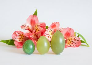 three jade green kegel balls on a white surface with flowers in the background
