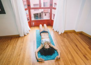 woman lying on a yoga mat in front of bay windows doing pelvic exercises