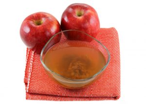 bowl of unfiltered apple cider vinegar including the mother and two red apples