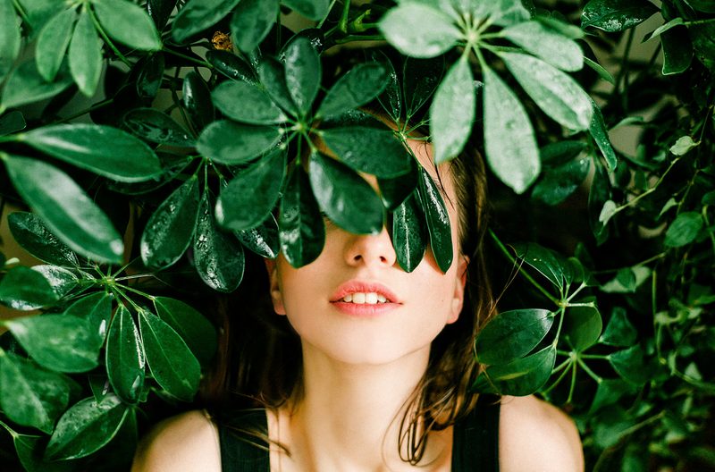 Woman's face covered by green leaves