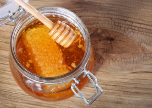 raw honey and honey dipper in jar on a table