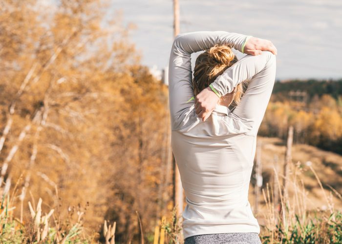 slender woman stretching with one arm behind her head