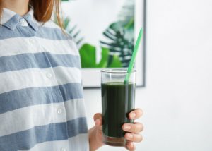 woman holding a tall glass of spirulina drink with a straw