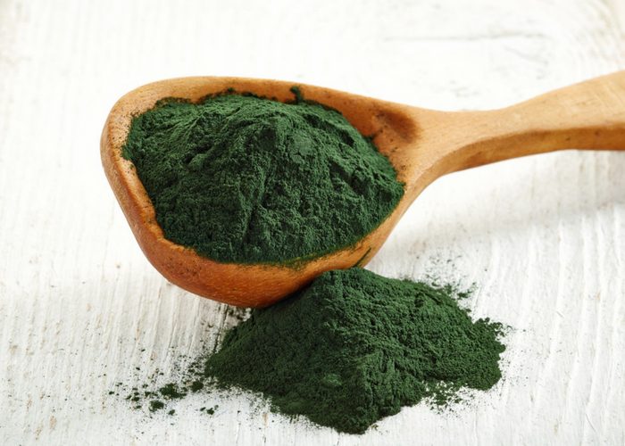 spirulina powder spilling out of a wooden spoon
