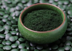 spirulina powder in a dark green bowl surrounded by spirulina tablets