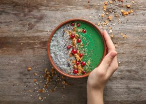woman's hand holding a spirulina smoothie bowl on a wooden background