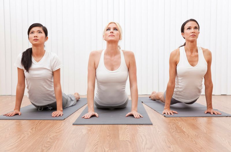 Three women dressed in white doing yoga cobra pose
