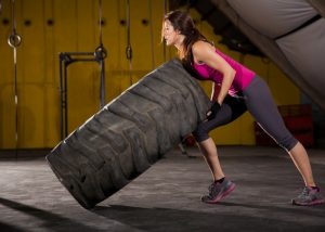 a woman in fitness gear lifting a large rubber tire