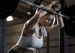 a woman in white sports bra leaning forward on a weightlifting bar
