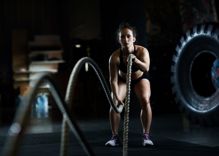a fit woman doing battle rope exercises in a dark gym