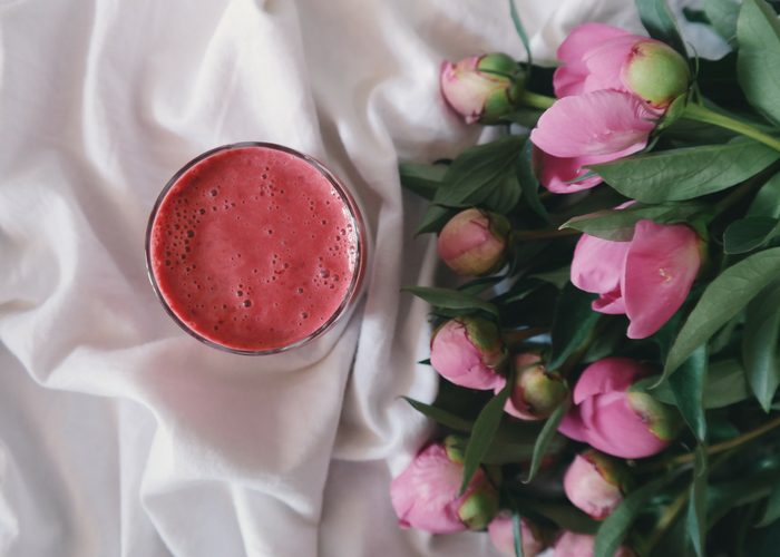red superfood smoothie on white linen and a bunch of pink flowers beside it