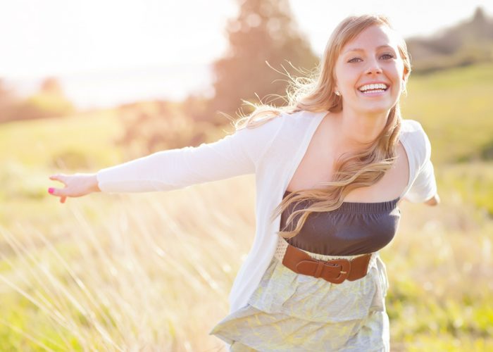 a smiling and confident woman with outstretched arms in a field