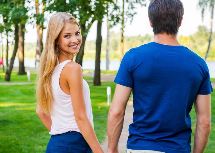confident woman looking at the camera smiling while holding her boyfriend's hand
