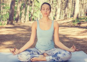 a woman sat in a meditation pose in the woods