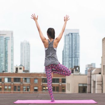 Woman on a rooftop standing on a pink yoga mat in a yoga pose
