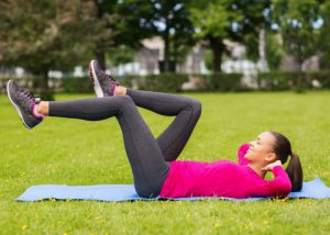 a young woman laid on a pilates mat outdoors performing pilates leg circles